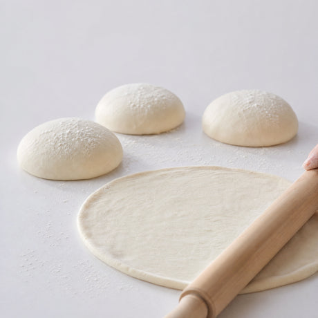 Romana Tonda pizza dough balls with one rolled out thin, showing the characteristic thin Roman-style base