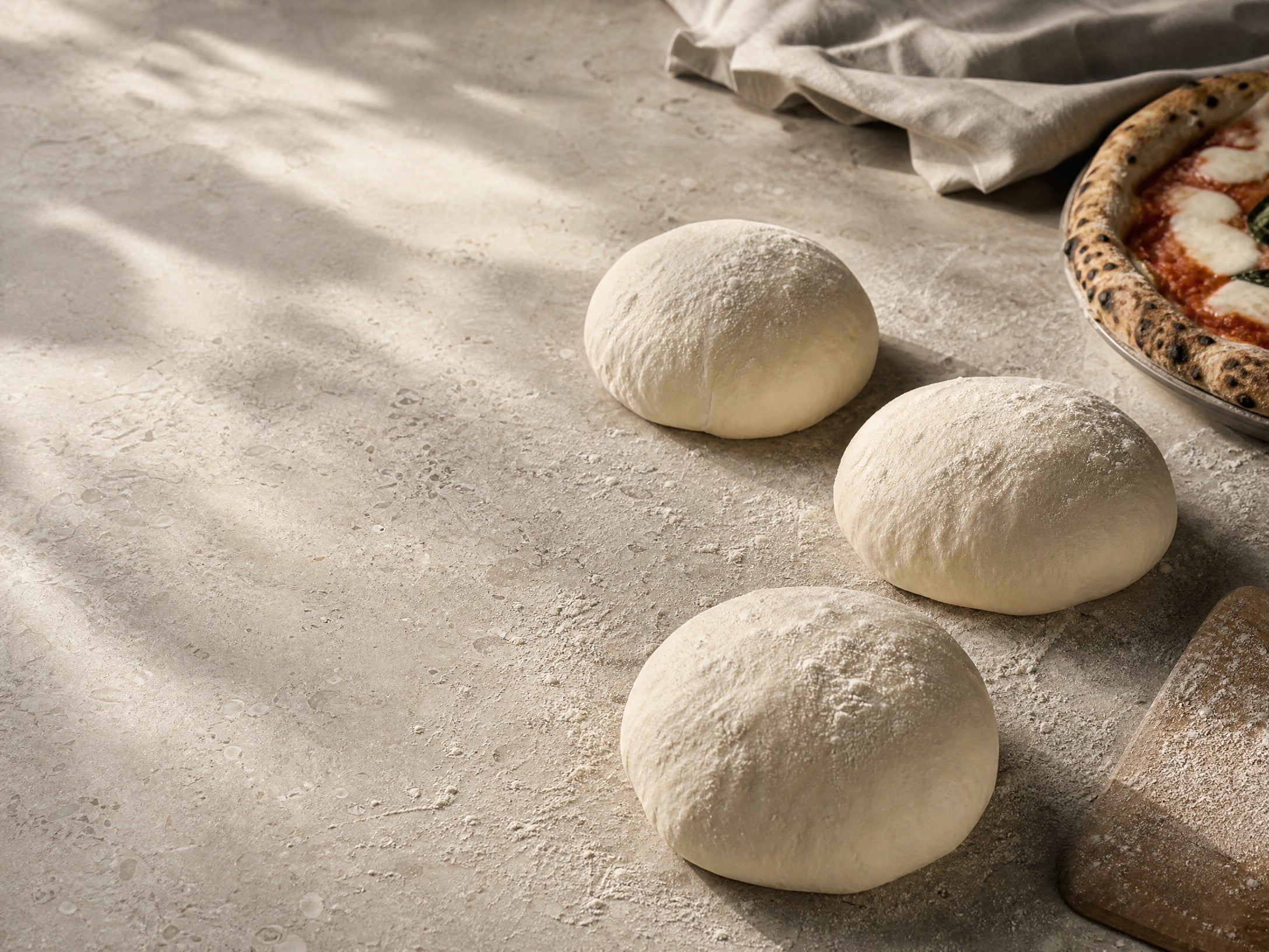 Fresh pizza dough and a finished Neapolitan pizza on a flour-dusted worktop